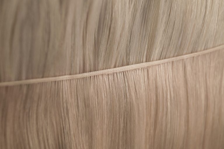 Nahaufnahme einer hochwertigen, blonden Premium‑Tresse zur Haarverlängerung: fein vernähte Kante, seidig fallende Strähnen mit natürlichem Glanz