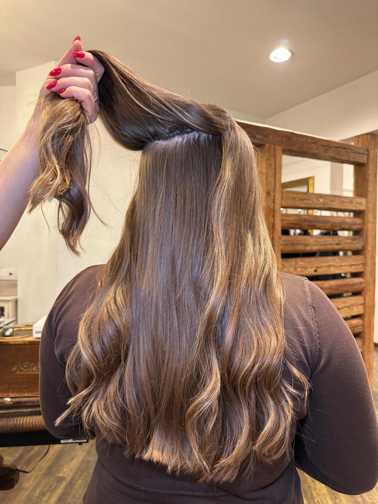 Was kostet eine Haarverlängerung. Eine Friseurin hebt die Haarverlängerung ihrer Kundin hoch, um sie zu zeigen.