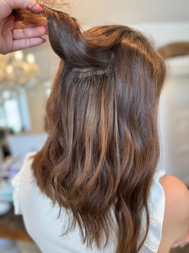 Aufnahme, die zeigt, wie man Tressen einnähen kann. Auf dem Bild ist eine braune Tresse für die Haarverlängerung und Haarverdichtung mit Beach Waves im Summer Look zu sehen. Extensionspflege im Sommer in Bad Tölz